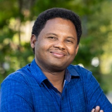 Man standing outside, wearing blue shirt. 