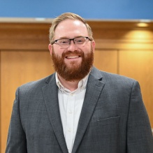 Man wearing suit, standing in a hallway. 