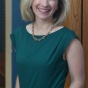 Woman in a green dress, smiling, standing in a hallway. 