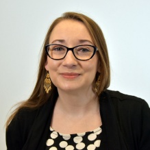 Woman wearing glasses, black jacket, smiling. 