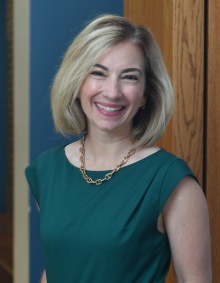 Woman in green dress, smiling, standing in a hallway. 