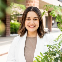 Woman standing outside nexst to brick building, smiling, green plant nexdt to her. 