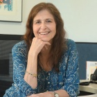 Woman wearing blue dress, sitting at her desk, smiling. 