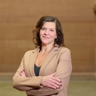 Woman wearing beige suit, arms crossed, smiling, standing in a large stairwell. 