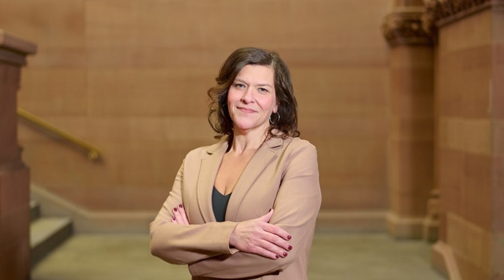 Woman wearing beige suit, arms crossed, smiling, standing in a large stairwell. 