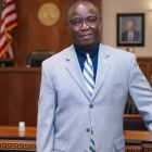 Man standing in a courtroom, wearing a blue suit. 