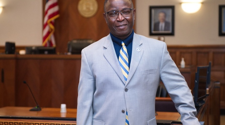 Man standing in a courtroom, wearing a blue suit. 