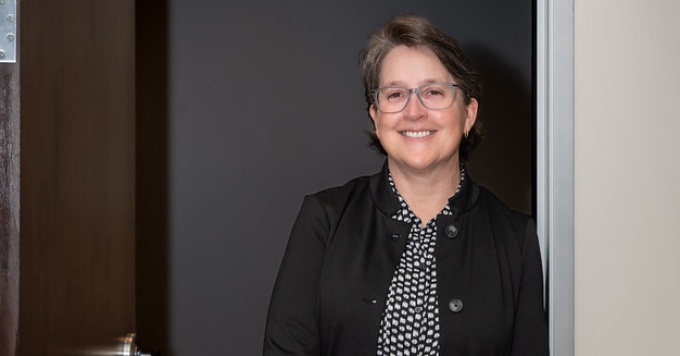 Woman wearing glasses, standing in a doorway. 