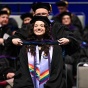 A young woman wearing graduation regalia receiving her stole from a member of the faculty during commencement. 