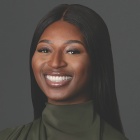 Person wearing a dark green high-neck top with long sleeves, posed against a plain dark gray background. The individual has straight, long dark hair parted in the center.