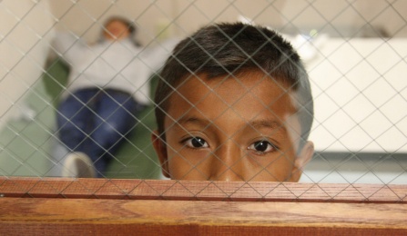 A boy looks out the door window from the room he is staying in at the Brownsville, Texas, port of entry. Photo by Edwardo Perez, courtesy of U.S. Customs and Border Protection.