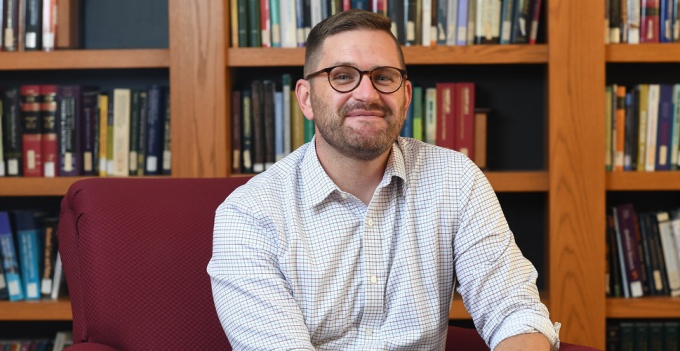 stark sitting in a room with books on a shelf.