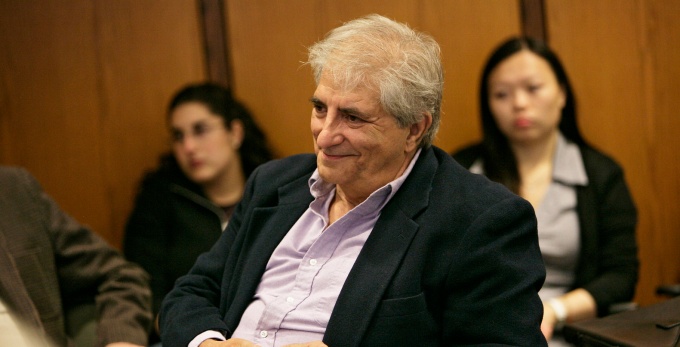 man sitting in a room. two students in the background.