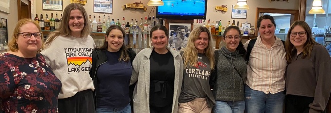 group of students standing in front of a bar.