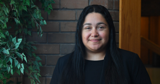 student outside a brick building, next to a leafy bush.