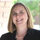 woman, standing outside next to a brick wall, smiling.