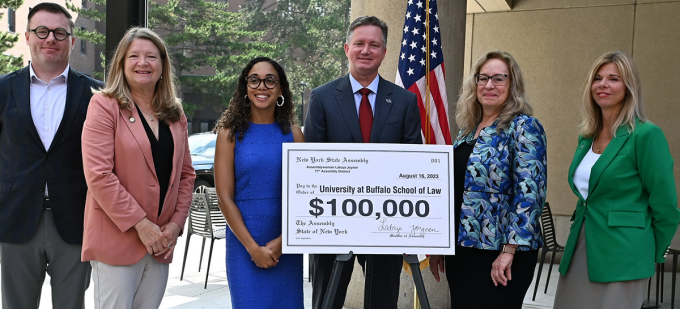 group of people standing smiling with a giant bank check that says $100,000.