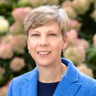 woman smiling, flower bushes behind her.
