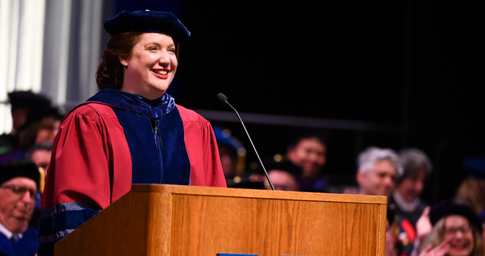 woman in red regalia standing at a podium, smiling.