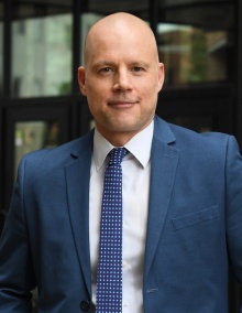 man smiling, standing outside a building.