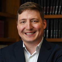man smiling standing in front of bookshelves.