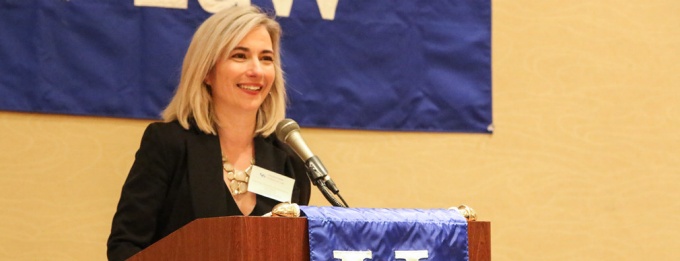 woman standing at a podium, speaking for an event.