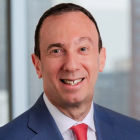 man smiling, standing in front of a window in a highrise building.