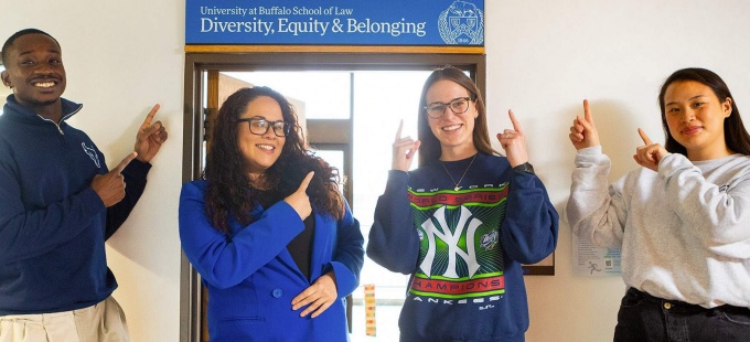 four people standing in front of a doorway, pointing at a sign that says Diversity, Equity & Belonging.