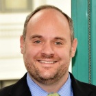 man in front of a window of an office window, smiling.