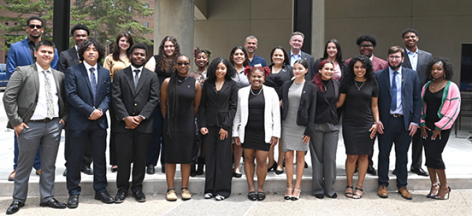 photo of a group of young adults standing together, smiling, outside in front of a building. 