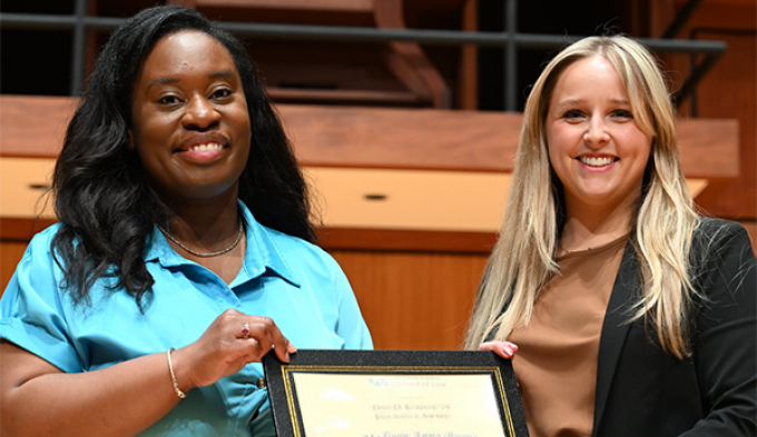 two women smiling, holding up an award. 