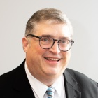 man wearing businesss suit and glasses, smiling. 