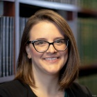 woman standing in front of bookcase, smiling. 