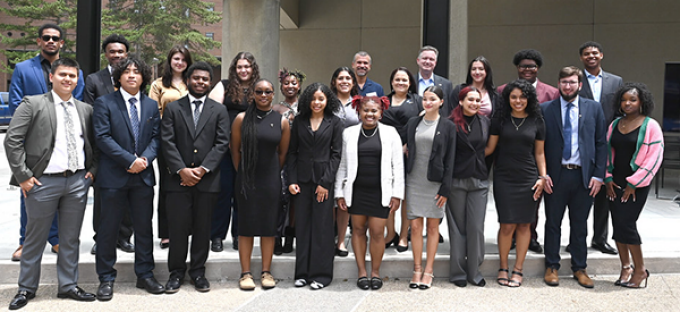 photo of a group of young adults standing together, smiling, outside in front of a building.