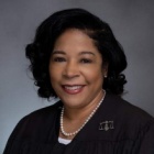 woman, smiling, wearning black robes and pearl necklace. 