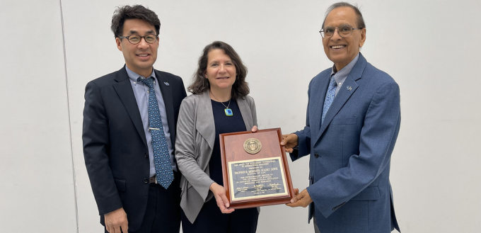 Woman standing between two men, holding a large plaque. 