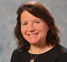 Woman smiling, wearing black top with gold necklace. 