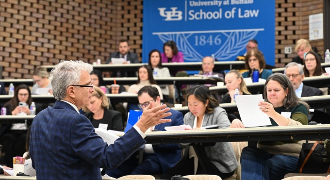 Man addressing a large classroom of individuals. 