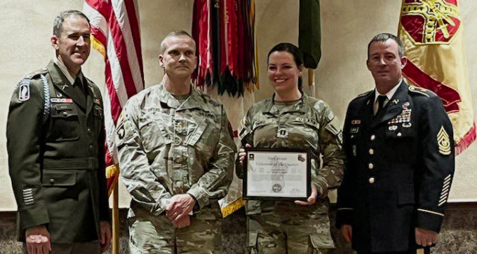 group of military people standing in front of flags, one holding up a certificate.