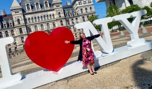 woman outside in front of a large sculpture that says "I *heart* N Y". 