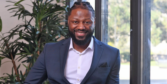 man smiling, standing next to a large window.
