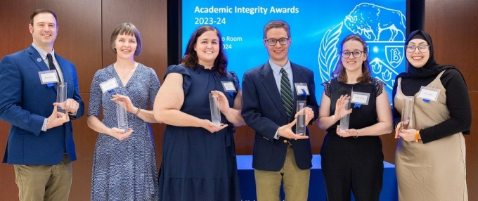 group of individuals standing in a line, holding their awards, smiling. sign behind them reads Academic Integrity Awards. 