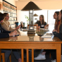 A group of students in a library, sitting around a table, talking. 