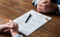 Partial view of lawyer and client sitting at wooden table with divorce decree and wedding rings. 