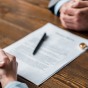 Partial view of lawyer and client sitting at wooden table with divorce decree and wedding rings. 