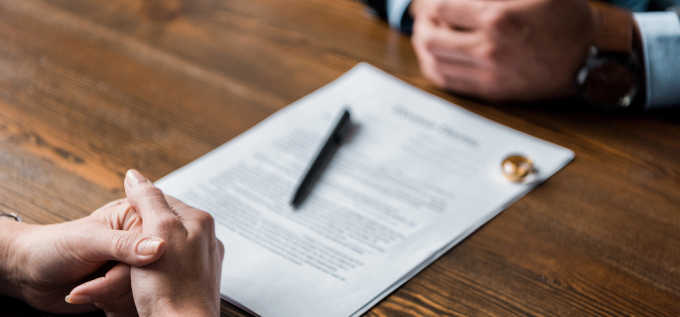 Partial view of lawyer and client sitting at wooden table with divorce decree and wedding rings. 