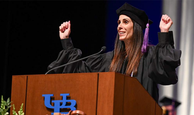 Young female graduate standing on state, behind a podium, smiling.