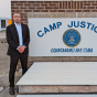 man standing outside next to a sign that says Camp Justice Guantanamo Bay, Cuba. 