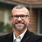 man standing outside, arms folded, smiling. 