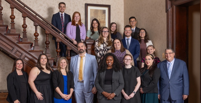 A smaller group of people, smiling, standing in front of, and on, a stairway.